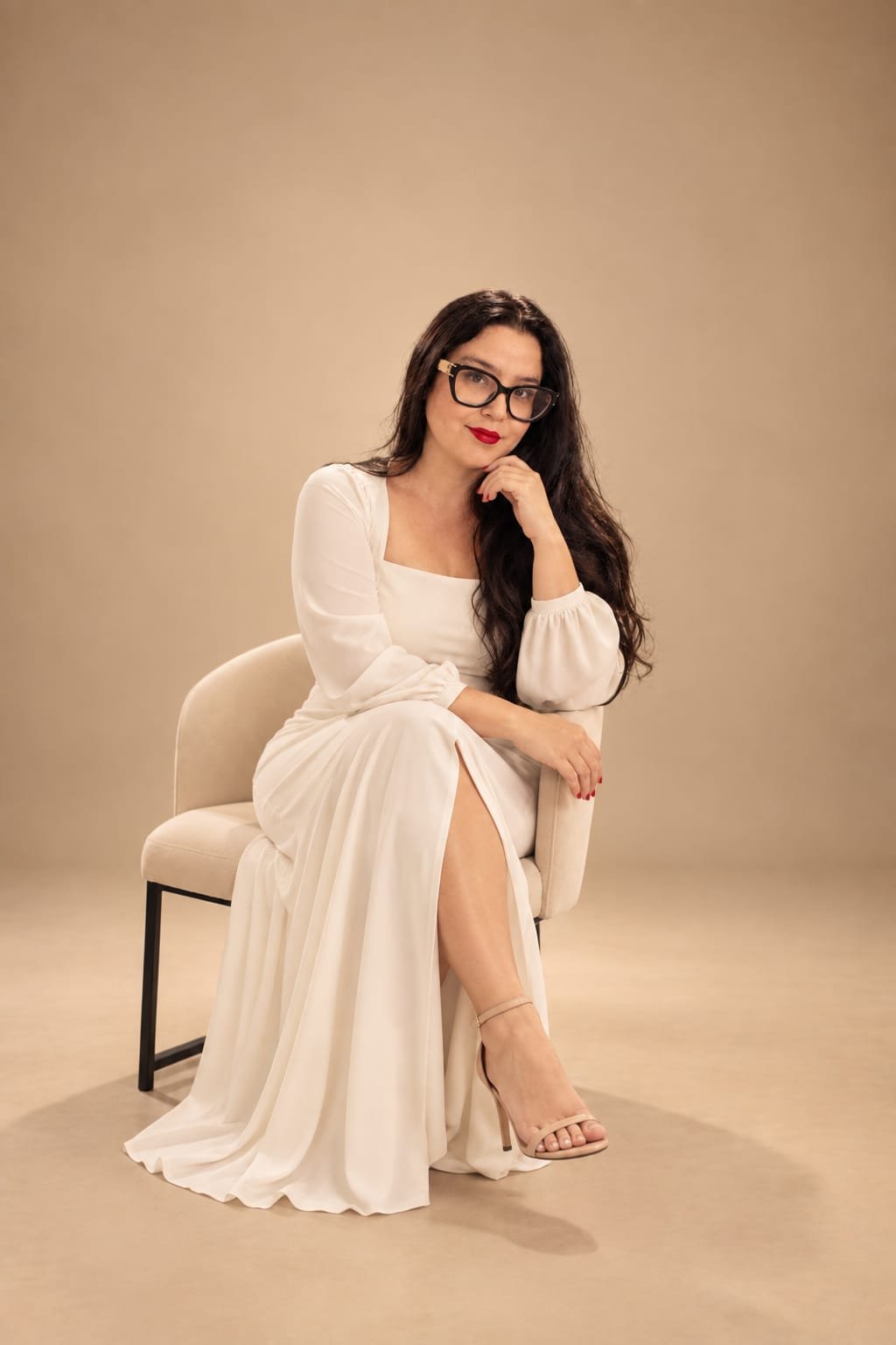 Bruna Lua, fundadora da Escola BY BL, sentada com vestido branco e batom vermelho